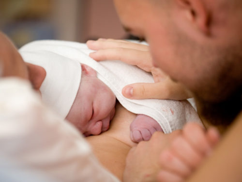 newborn on mother's chest with dad patting baby's back