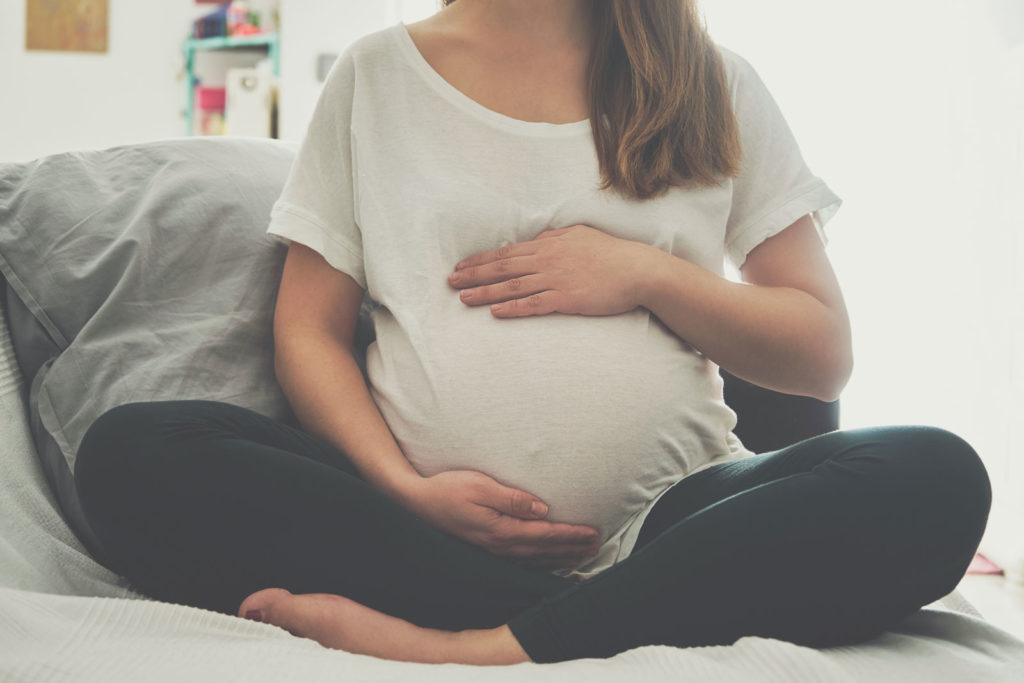 Pregnant woman sitting cross-legged and holding her belly.
