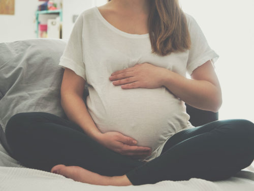 Pregnant woman sitting cross-legged and holding her belly.