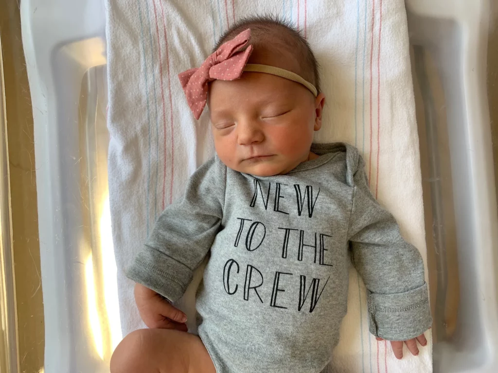 Maggie in a gray onesie that says "New to the Crew"