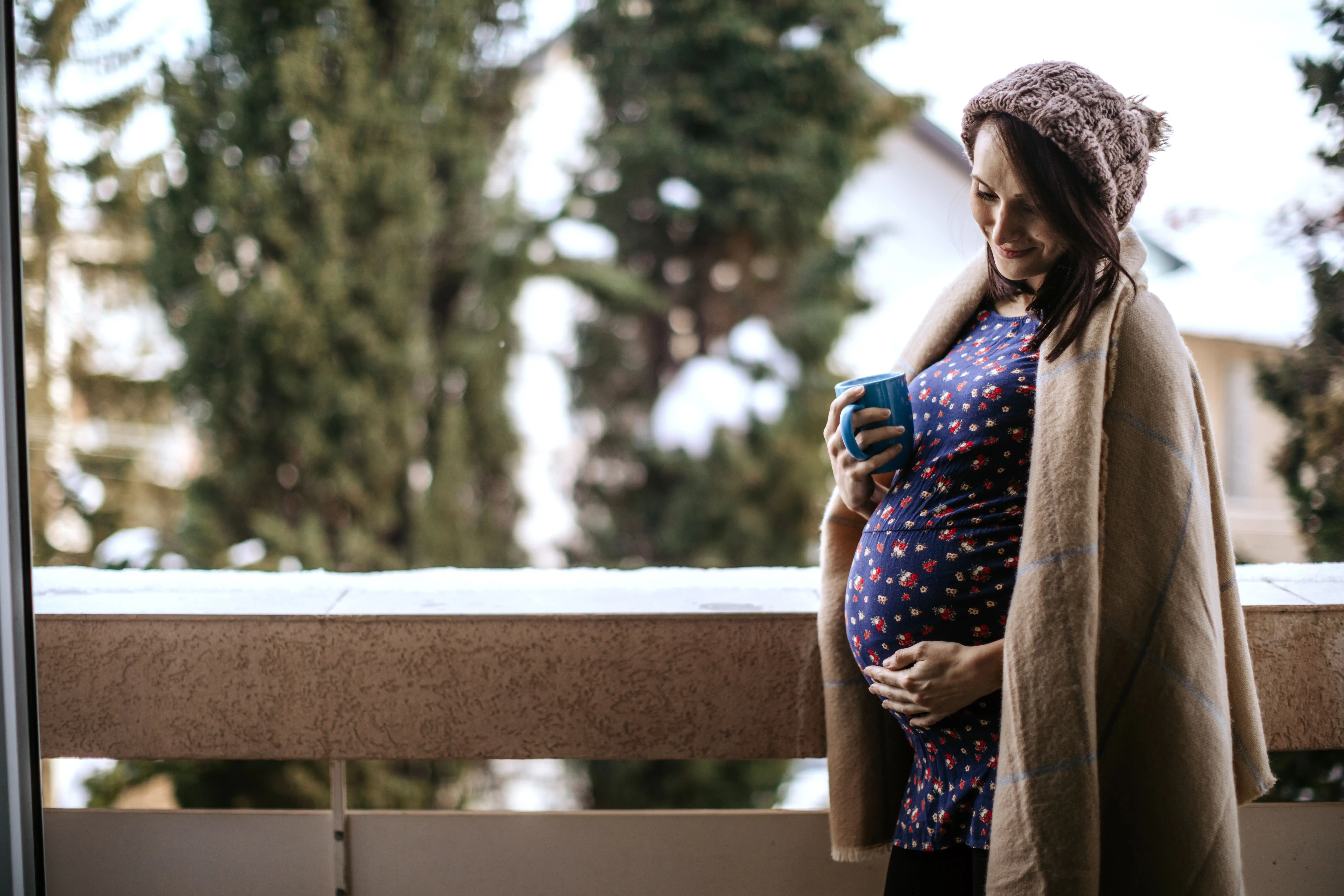 Pregnant woman drinking tea outside and holding her belly.